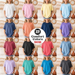 Könnte beinhalten: Eine Kollektion von kurzärmeligen T-Shirts mit Rundhalsausschnitt in 29 verschiedenen Unifarben, mit einer zentralen kreisförmigen Grafik und dem Text 29 Colors Comfort Colors 9018. Die T-Shirts sind in einem Raster angeordnet.