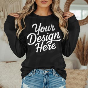May include: Black long-sleeve sweatshirt with the text "Your Design Here" in white script. The sweatshirt is paired with blue denim shorts. The image is a product mockup, perfect for showcasing custom designs.