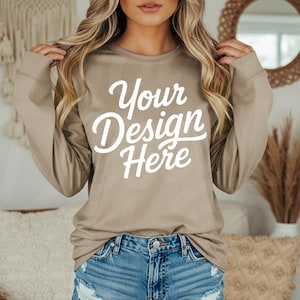 May include: A long-sleeved, tan-colored shirt with the text "Your Design Here" in white script. The shirt is paired with blue denim shorts. The overall style is casual and comfortable.