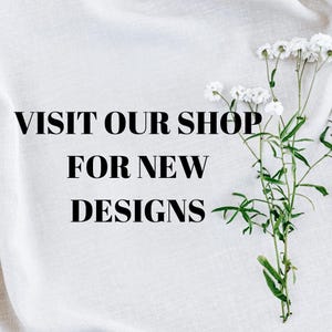 May include: White fabric background with the text "VISIT OUR SHOP FOR NEW DESIGNS" in black. A sprig of white flowers with green stems and leaves is on the right side of the image.