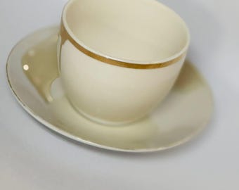 May include: A white teacup with a gold band around the rim sits on a matching saucer. The cup and saucer are both made of ceramic.