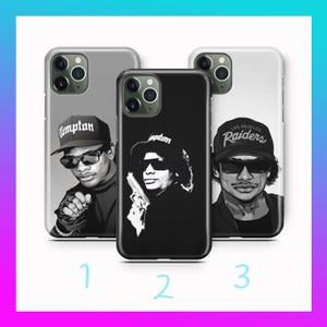 May include: Three phone cases with black and white graphics. The cases feature portraits of people wearing sunglasses and hats. One case has the word "Compton" on the hat, another has a person holding a gun, and the third has "Los Angeles Raiders" on the hat.