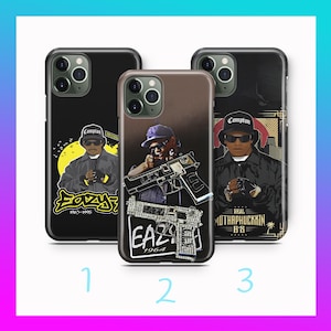 May include: Three phone cases with different designs. One case is black with a yellow sun and the text "Eazy" and "1963-1995". Another case is brown with a person holding a gun and the text "EAZY 1964". The third case is black with the text "Compton".