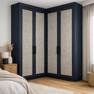 May include: A navy blue corner wardrobe with four doors. The door panels are a light beige fabric. The wardrobe has black handles. The room has a light beige rug and wooden floors. A bed and nightstand are in the foreground.