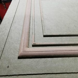 Puede incluir: Primer plano de un panel de madera gris claro con un marco rectangular empotrado. El marco es de un tono marr&oacute;n m&aacute;s oscuro y tiene un borde redondeado en relieve. El panel parece inacabado.