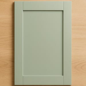 Puede incluir: Una puerta de armario verde salvia con un diseño de panel empotrado. La puerta es rectangular con un marco alrededor del panel central. El fondo es una superficie de veta de madera clara.