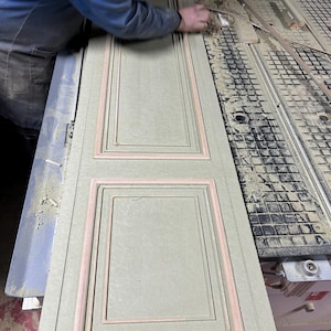 Puede incluir: Un panel de madera verde claro con un dise&ntilde;o rectangular empotrado y ribete rosa. Una persona con una camisa azul est&aacute; trabajando en el panel. El panel est&aacute; cubierto de serr&iacute;n.