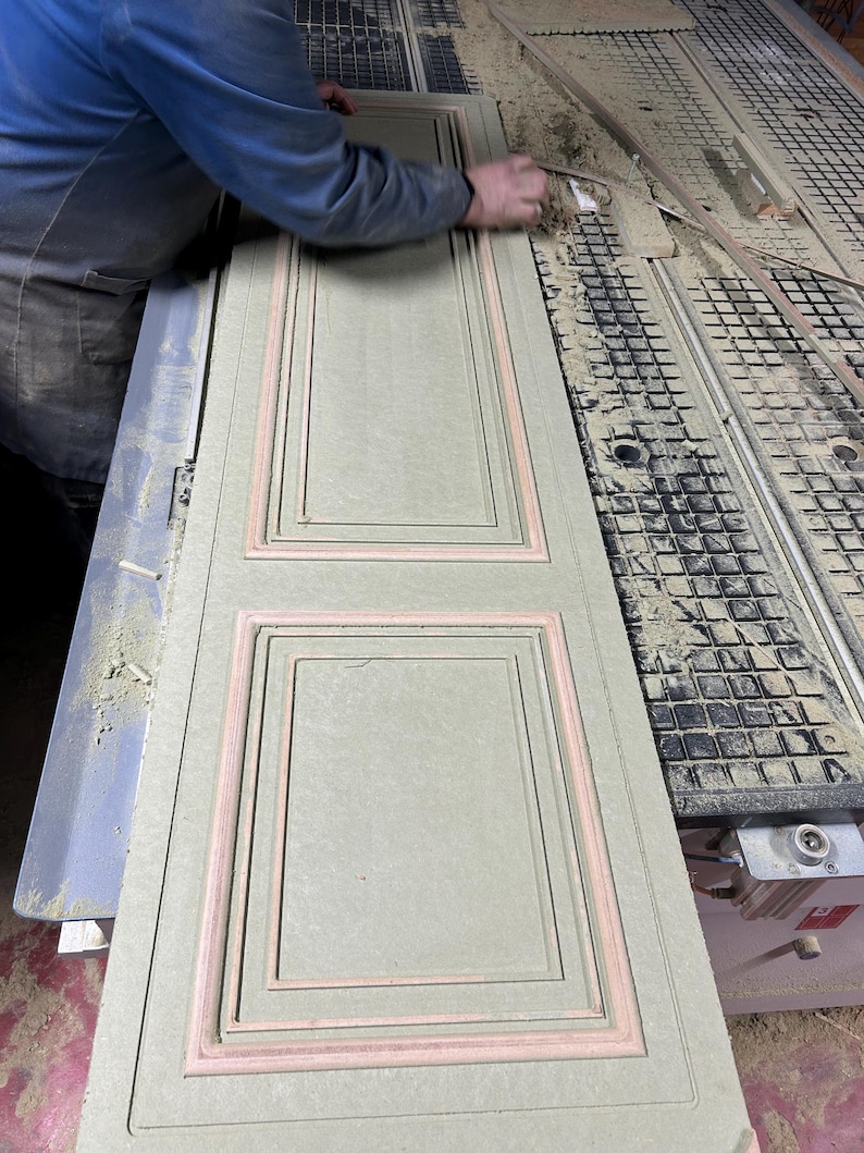 Puede incluir: Un panel de madera verde claro con un dise&ntilde;o rectangular empotrado y ribete rosa. Una persona con una camisa azul est&aacute; trabajando en el panel. El panel est&aacute; cubierto de serr&iacute;n.