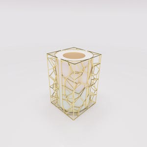 Puede incluir: Un jarrón decorativo moderno con un diseño geométrico de jaula de metal dorado. El interior del jarrón es de color rosa claro, con una base blanca. La parte superior del jarrón es de color beige claro.