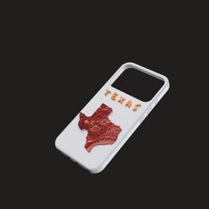 May include: White phone case featuring a raised red Texas state outline and the word "TEXAS" in gold letters. The case has a white border and is set against a dark background.