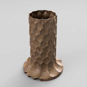 Op de afbeelding: Een hoge houten vaas met een uniek honingraatpatroon dat in het oppervlak is gesneden. De vaas heeft een uitlopende basis en een gestructureerd, geometrisch ontwerp, met natuurlijke houttinten. De bovenrand heeft een geschulpte vormgeving.