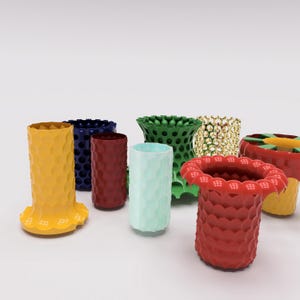 Puede incluir: Una colección de jarrones coloridos con diversos diseños. Los jarrones, en tonos amarillo, azul, rojo, verde y dorado, presentan patrones de panal y perforados. Algunos tienen un borde con volantes, ofreciendo una variedad de estilos.