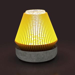 Puede incluir: Una lámpara de mesa moderna con una pantalla cónica amarilla hecha de listones verticales. La pantalla se asienta sobre una base gris y circular. La lámpara emite un brillo cálido y acogedor, sugiriendo un ambiente acogedor. La parte superior de la lámpara tiene una superficie clara y texturizada.