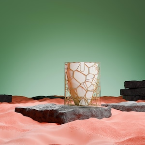 May include: A white geometric object with a gold wire frame sits on a black rock in a bed of pink sand. The background is a solid green.
