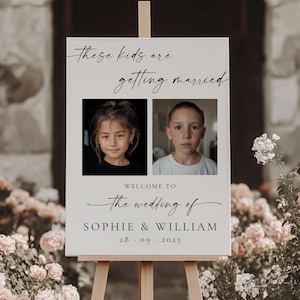 Op de afbeelding: Een welkomstbord voor een bruiloft op een houten ezel. Het bord heeft twee foto's van kinderen en de tekst: "These kids are getting married" en "Welcome to the wedding of Sophie & William 28.09.2025".