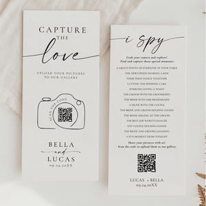 May include: Two white wedding signs with black text. One sign reads "Capture the Love" and includes a camera graphic with a QR code. The other sign says "i spy" and lists wedding photo ideas. Both signs include names and a date.