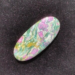 May include: An oval-shaped gemstone with a mix of colors. The stone features a base of green and white with patches of pink and yellow. The stone is smooth and polished, with a natural, organic appearance.