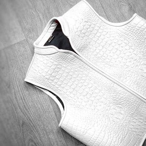 "Luxury white crocodile leather vest displayed on wooden floor, showcasing premium exotic skin texture, high-end fashion craftsmanship, and elegant sleeveless design. Ideal for men's designer outerwear, upscale streetwear, or formal luxury wardrobe collection."