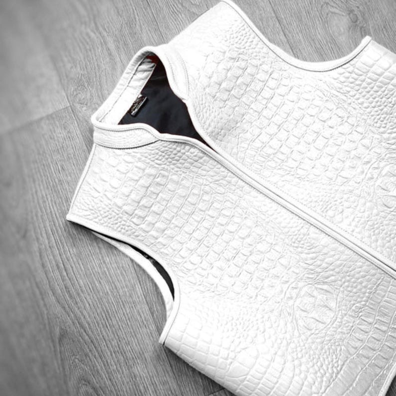 "Luxury white crocodile leather vest displayed on wooden floor, showcasing premium exotic skin texture, high-end fashion craftsmanship, and elegant sleeveless design. Ideal for men's designer outerwear, upscale streetwear, or formal luxury wardrobe collection."