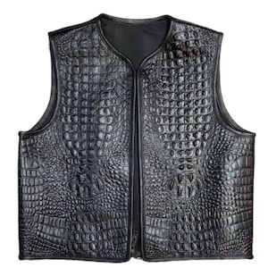 May include: A black, sleeveless vest with a textured, crocodile-skin pattern. The vest has a V-neck and a full-length zipper down the front. The material appears to be leather or a leather-like material. The vest is designed to be worn as an outer layer.
