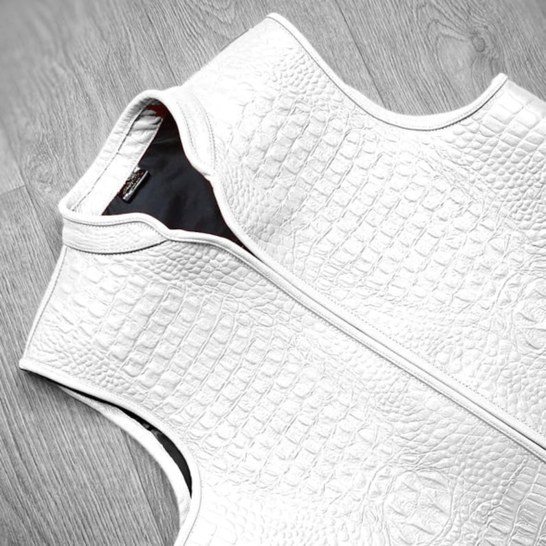 "High-resolution image of white crocodile leather vest laid flat on wooden surface, emphasizing rich exotic texture, luxury finish, and designer craftsmanship. A statement piece for men's high-fashion, premium streetwear, or custom tailored wardrobe essentials."
