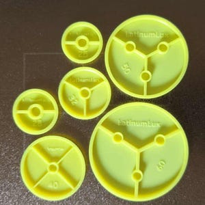 May include: A collection of seven yellow plastic discs of varying sizes. Each disc has a central hole and is marked with a number, ranging from 25 to 60. The brand name "LatinumLux" is printed on some of the discs. The discs have a three-pronged design.