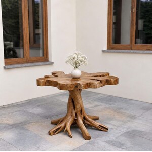 May include: A round table crafted from a single piece of light brown wood with a natural, irregular edge and a base formed by thick, gnarled tree roots. A small, white, spherical ceramic vase containing white baby's breath flowers sits on top.
