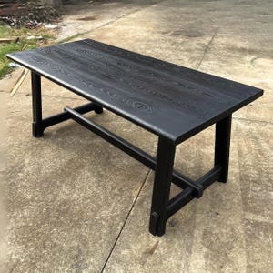 May include: A rectangular black wooden table with a textured surface. The table has four legs and a supporting beam connecting the legs. The table's dimensions are approximately 72 inches long, 36 inches wide, and 30 inches high.