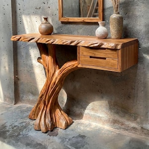 May include: A wooden console table featuring a live-edge top and a base carved from a single tree trunk. The table includes a rectangular section with two horizontal drawers. On the surface sit a round brown vase, a white vase, and a tall textured vase.