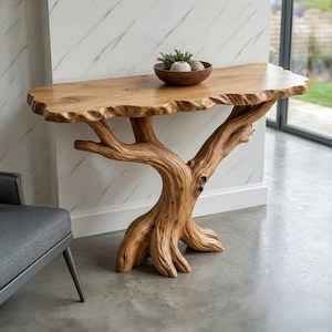 Puede incluir: Una consola de madera natural con una encimera de borde vivo. La base está elaborada para parecer un tronco de árbol y ramas. Un cuenco de madera con piedras decorativas y vegetación se encuentra sobre la mesa.