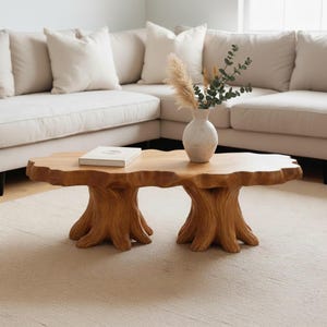 May include: A wooden coffee table with a tree trunk base and a freeform top. The table is in a living room setting with a white sofa, a vase with dried plants, and a book. The table is made of natural wood.