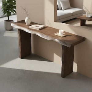 Puede incluir: Una consola de madera maciza marrón oscuro con borde natural y forma orgánica. Un jarrón blanco con una ramita, un libro y una vela en una bandeja pequeña se exhiben en la mesa. Diseño moderno.