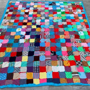 Könnte beinhalten: Eine große Patchwork-Decke aus verschiedenen bunten Stoffen. Die Decke besteht aus Quadraten unterschiedlicher Größe und Farbe und ist mit einem blauen Rand zusammengenäht.