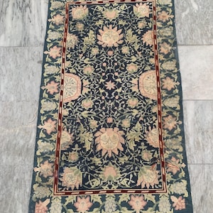 Könnte beinhalten: Ein rechteckiger Teppich mit dunkelblauem Hintergrund und einem Blumenmuster in Rosa-, Grün- und Cremetönen. Der Teppich hat einen roten Rand und ein detailliertes Design, geeignet für die Inneneinrichtung.