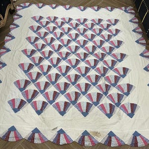 May include: A white quilt with a scalloped edge and a repeating pattern of blue, pink, and white fan shapes.