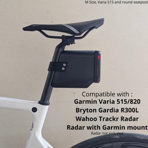 Op de afbeelding: Een zwarte zadelpenhouder voor radarapparaten, bevestigd aan een wit fietsframe onder een zwart zadel. Tekst: M Size, Varia 515 and round seatpost. Compatible with: Garmin Varia 515/820, Bryton Gardia R300L, Wahoo Trackr Radar, Radar with Garmin mount.