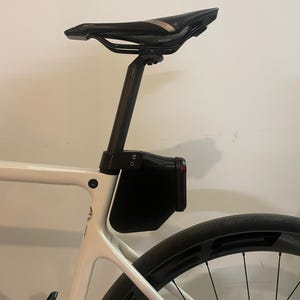 Puede incluir: Bicicleta de carretera blanca con sillín, tija y neumático trasero negros. Una caja de almacenamiento negra está montada debajo del sillín. La bicicleta tiene un diseño elegante y moderno, adecuada para el ciclismo.
