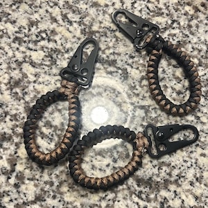 May include: Three black paracord keychains with black metal clips. The paracord is woven in a black and brown pattern.