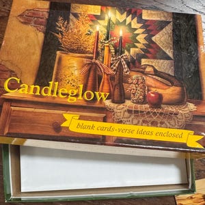 May include: A box of "Candleglow" blank cards with verse ideas enclosed. The box features a rustic illustration of lit candles, a wooden bowl, and a red apple. The background includes a quilt and a brick wall.