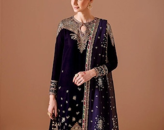 May include: A dark purple velvet salwar kameez set with gold embroidery. The ensemble includes a long-sleeved tunic, matching pants, and a sheer dupatta. The outfit features intricate gold detailing around the neckline, cuffs, and hem.