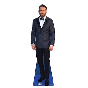 May include: A life-size cardboard cutout of a man wearing a dark gray double-breasted suit with a black bow tie and black dress pants. The cutout is standing on a blue base.