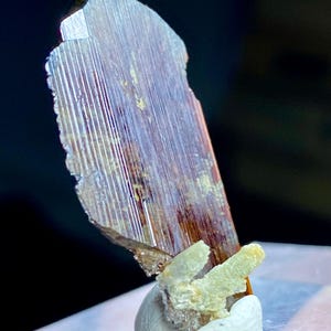 Puede incluir: Un gran espécimen mineral iridiscente marrón y dorado con estrías. El mineral está montado sobre una base blanca texturizada.