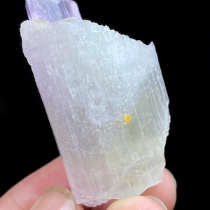 Puede incluir: Un cristal translúcido verde claro y rosa con estrías. El cristal tiene una pequeña inclusión amarilla.