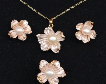 May include: A floral jewelry set featuring a necklace pendant, earrings, and a ring. Each piece has a flower design with a central pearl and gold-colored accents. The petals are a soft pink color, and the set is displayed on a black background.