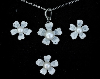 May include: A silver-toned jewelry set featuring a necklace with a flower pendant and matching flower earrings. Each piece has a flower design with a central pearl. The set is displayed on a black background.