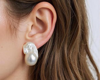 May include: A single baroque pearl earring with an irregular, organic shape and a high-luster, creamy white surface. The pearl features a smooth, rounded bottom section that transitions into a textured, rippled top portion attached to the earlobe.