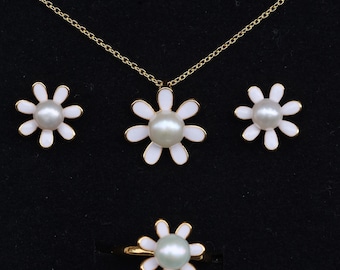 May include: A jewelry set featuring a daisy design. The set includes a necklace, earrings, and a ring. Each piece has a white enamel flower with a pearl center and gold-colored accents. The jewelry is displayed on a black background.