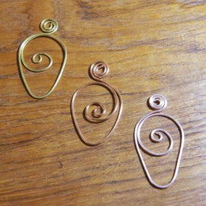 May include: Three handmade wire pendants in gold, copper, and silver tones. Each pendant features a teardrop shape with a spiral design in the center and a small coil at the top. The pendants are displayed on a wooden surface.
