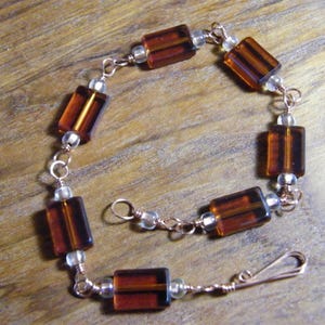 Op de afbeelding: Een koperen draad armband met bruine rechthoekige glazen kralen en kleine heldere kralen.