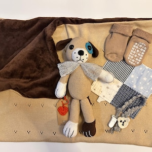 Puede incluir: Una manta de bebé de punto marrón y beige con un juguete de cachorro de ganchillo, un par de botines marrones y un cuadrado de tela de patchwork con un patrón de estrellas azules y blancas.